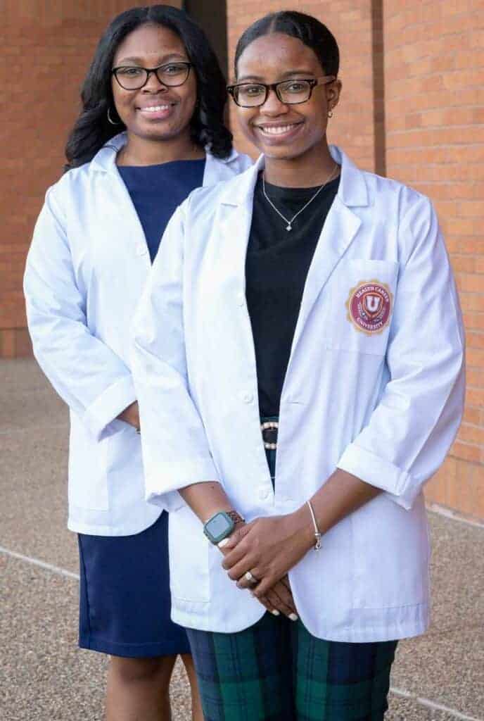 Two young women wearing lab coats and smiling.